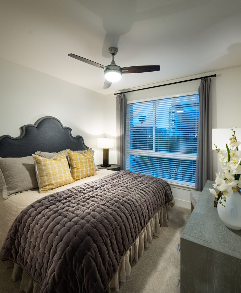 Bedroom with plush carpet, king sized bed, ceiling fan and large window