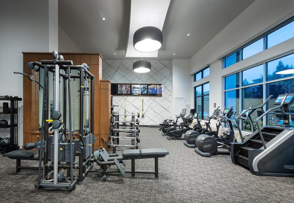 Fitness center with cardio machines, strength training equipment, flat screen TVS, and large windows