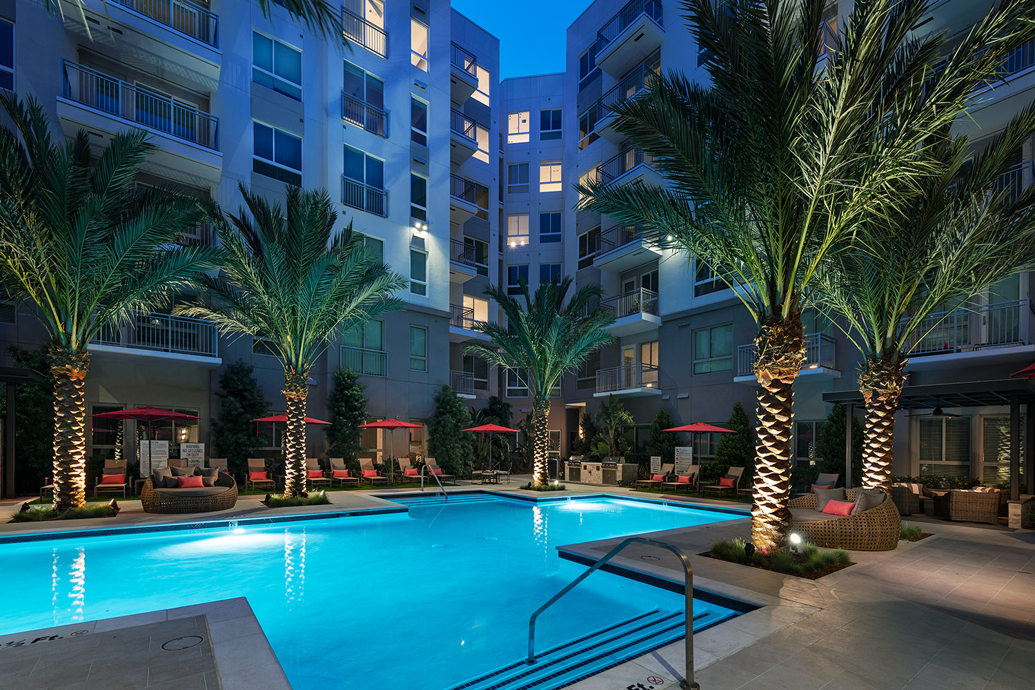 Resort style pool with lounge seating, umbrellas and tropical landscaping