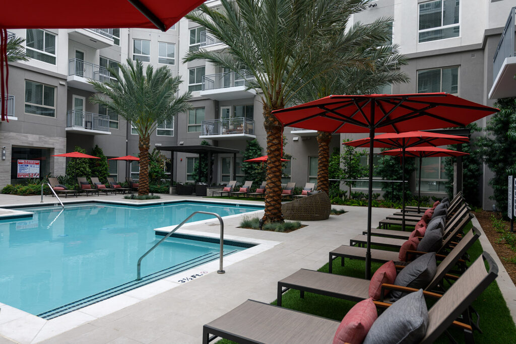 Resort style pool with rows of lounge seating, umbrellas and tropical landscaping